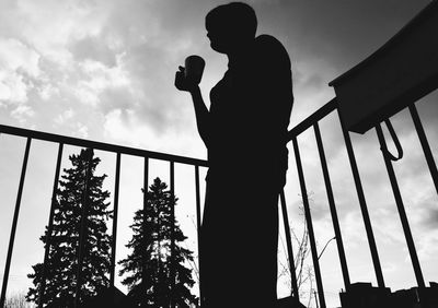 Low angle view of silhouette man standing by railing against sky