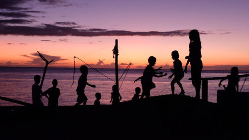 Silhouette people on beach against sky during sunset