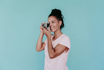 Young man holding camera while standing against gray background