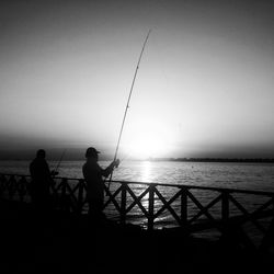 Silhouette men fishing in sea at dusk