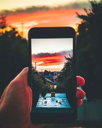 Hand holding smart phone against sky during sunset