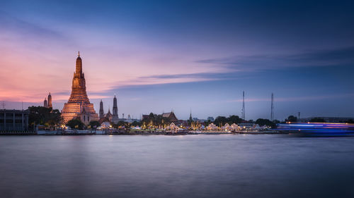 View of temple by river against cloudy sky at sunset