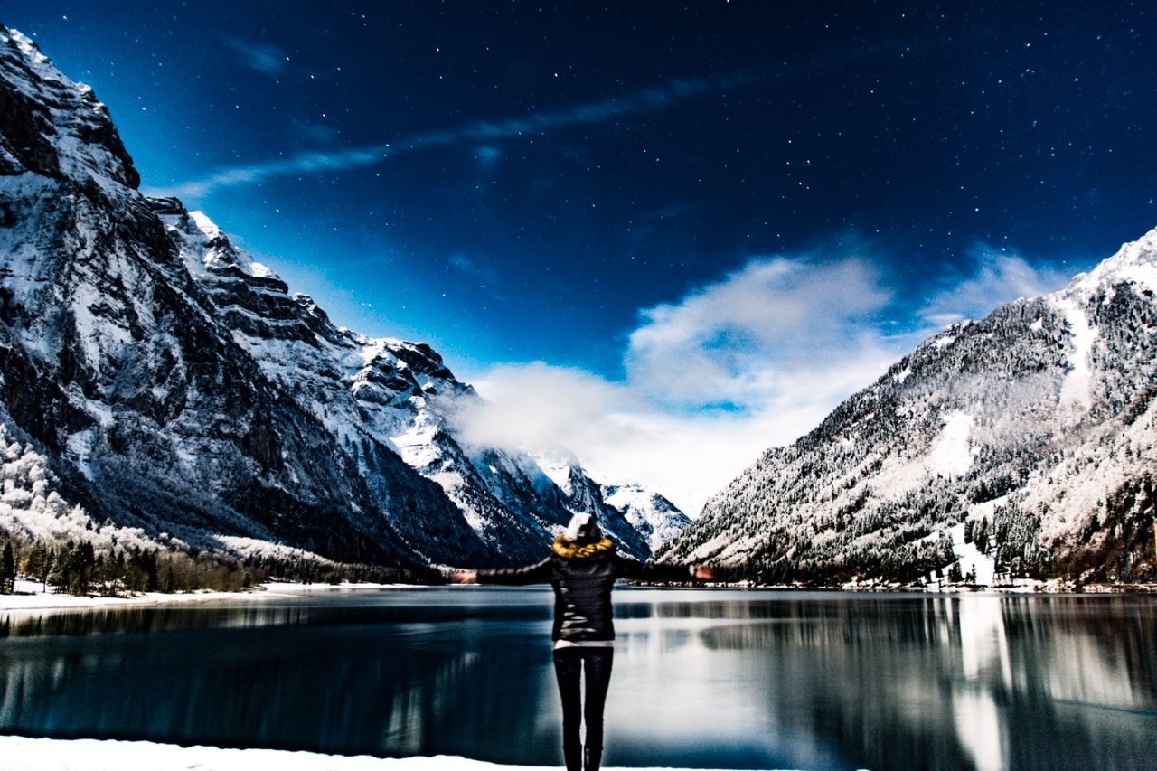 mountain, scenics - nature, beauty in nature, winter, mountain range, one person, real people, cold temperature, sky, snow, water, leisure activity, tranquil scene, lifestyles, non-urban scene, standing, tranquility, nature, snowcapped mountain, human arm, astronomy, outdoors