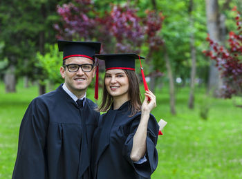 Portrait of smiling students in graduation gown standing in park