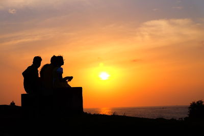 Silhouette friends sitting against sea during sunset