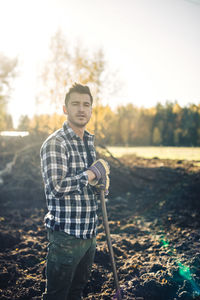 Portrait of confident male farmer with shovel standing on organic farm
