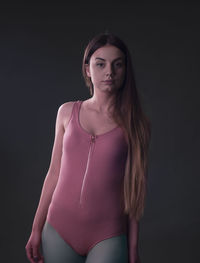 Portrait of young woman standing against black background