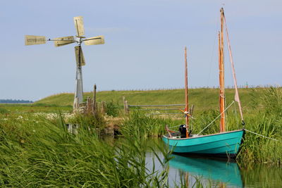 Boat moored on wooden post on field against sky