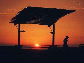 Silhouette man standing on beach against orange sky