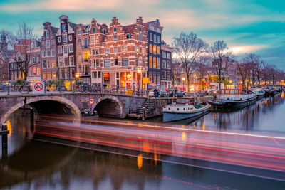 Light trails on bridge over river in city against sky