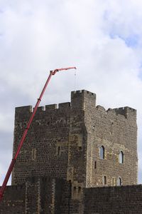 Low angle view of crane by building against sky