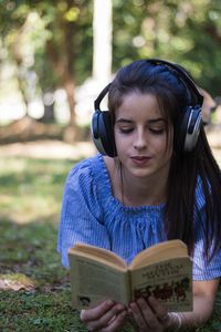 Portrait of young woman reading book on field