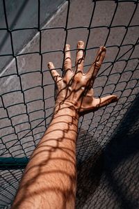 Hand with shadow shapes grabbing a metallic fence