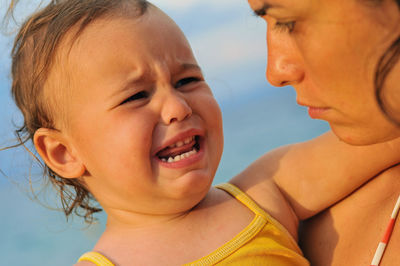 Close-up of mother looking at crying daughter against sky