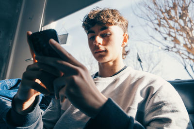 Low angle portrait of trendy teenager boy using mobile phone