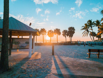 Palm trees by swimming pool against sky during sunset