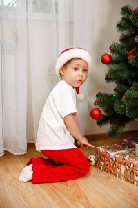 Boy in santas hat and pajamas found holds gift under christmas tree.