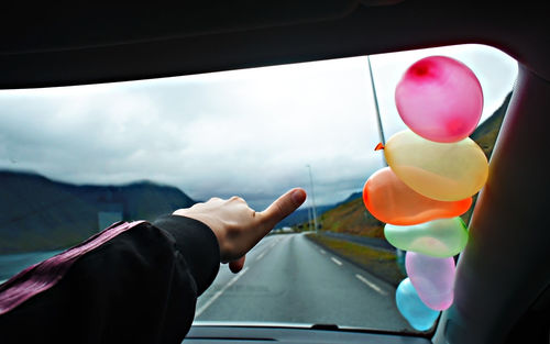 Traveling by car on mountain roads of iceland and thumbs up, colorful balloons on  glass of car hand