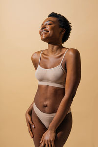 Portrait of young woman standing against yellow background