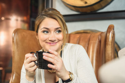 Delighted woman drinking beverage in armchair