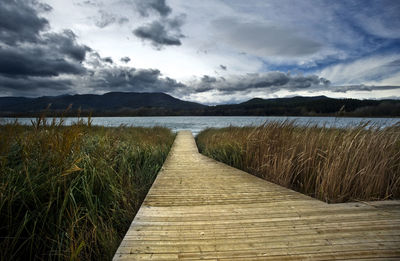 Boardwalk leading towards lake against sky