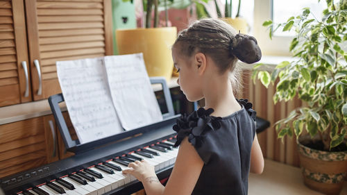 Rear view of girl playing piano at home