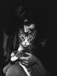 Portrait of woman with cat against black background