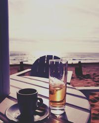 Close-up of beer on table at beach against sky