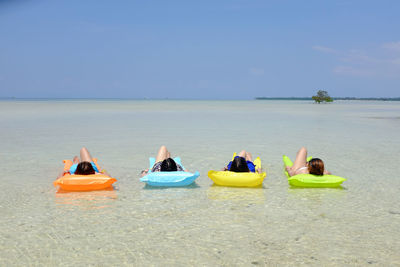 Women relaxing on inflatable rafts in sea against sky during sunny day