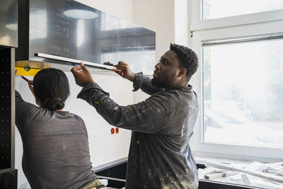 Multiracial male and female carpenters measuring cabinet with equipment in kitchen