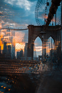 Bridge over illuminated city against sky during sunset