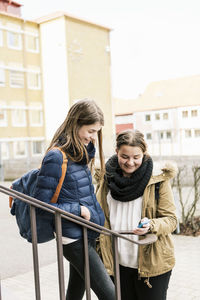 Happy young women using mobile phone outside school building