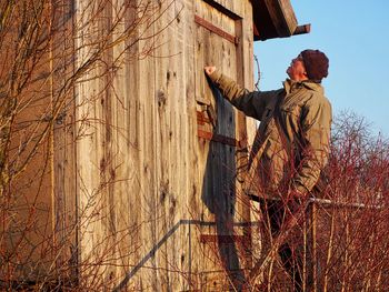 Man knocking log cabin standing against sky