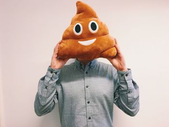 Man holding stuffed toy against face while standing by wall