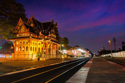 Illuminated railroad station by building against sky at night