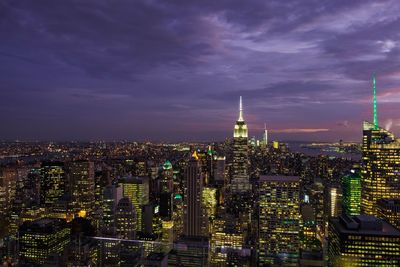 Illuminated empire state building with cityscape against cloudy sky during sunset