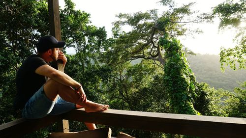 Side view of young man sitting on railing in balcony