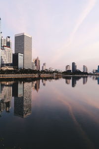 Reflection of buildings in city against sky during sunset