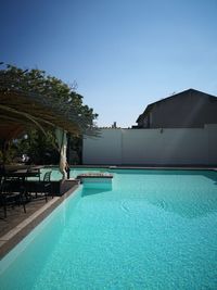 Swimming pool by trees against clear blue sky