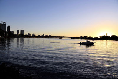 Silhouette cityscape by sea against sky during sunset