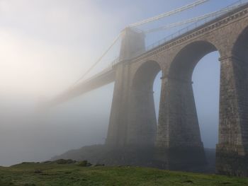 Low angle view of bridge against sky during foggy weather