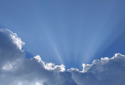 Low angle view of sunlight streaming through clouds