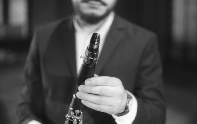 Midsection of man holding clarinet while standing at studio