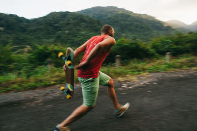 Full length of mid adult man skateboarding on mountain against sky