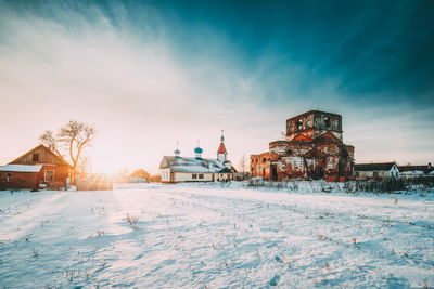 Snow covered field by buildings against sky