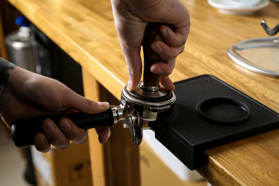 Cropped hands crushing coffee beans in portafilter at cafe