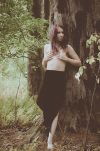 Portrait of young woman standing by tree in forest