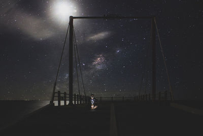 Silhouette man sitting on bridge against sky at night