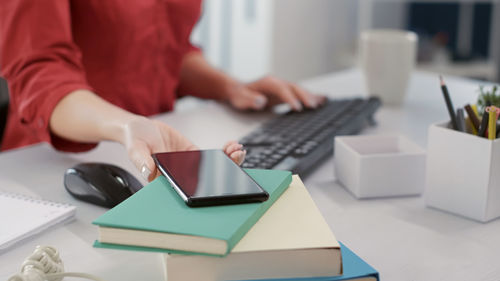 Midsection of woman taking mobile phone at desk