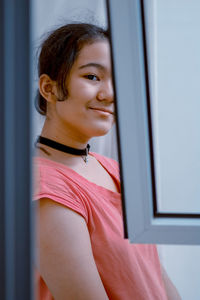 Portrait of smiling young woman looking through window at home